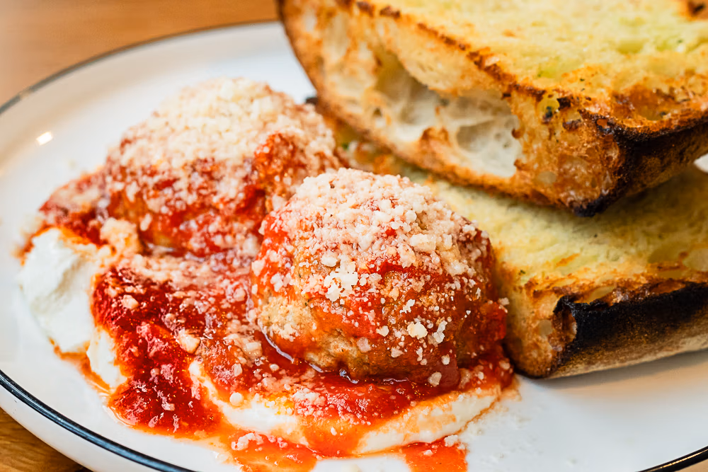 Meatballs on top of whipped ricotta with a side of garlic bread